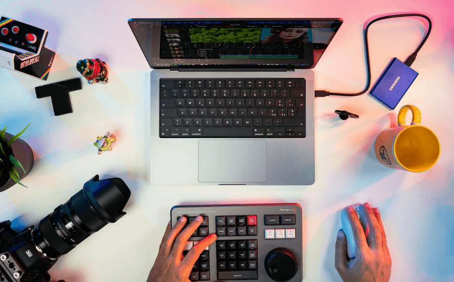An aerial view of hands working with a laptop, camera and editing tools to illustrate getting more Subscribers on YouTube