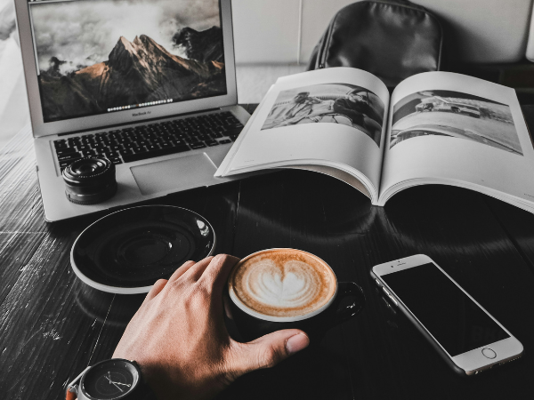 A man working in a coffee shop with his laptop, phone and camera to illustrate creating a Social Media Marketing Strategy